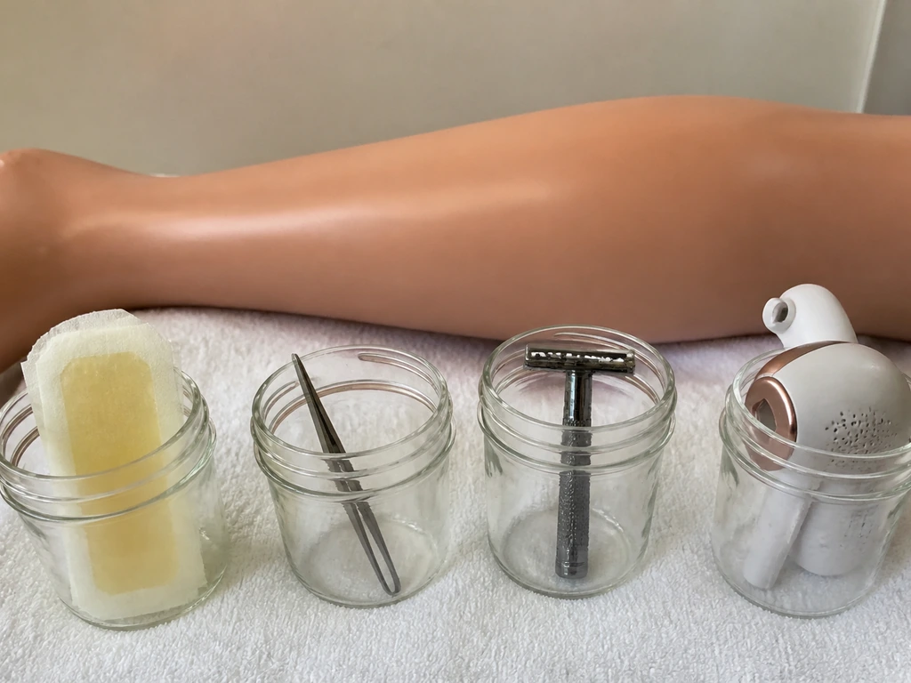 Row of hair-removal tools and wax, razor, tweezers, and laser beside smooth mannequin skin on a clean towel.